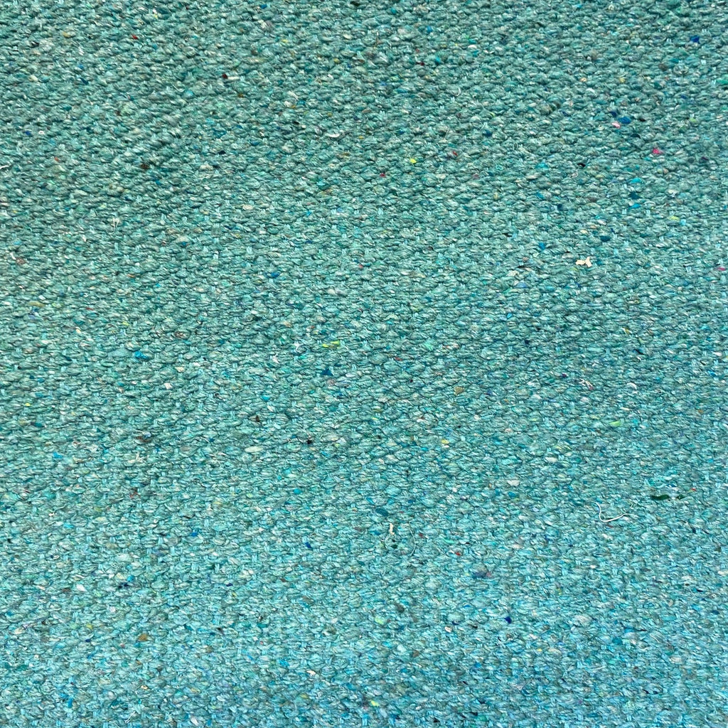 A close-up texture shot of a woven fabric or carpet in a mottled teal color, showing a dense, speckled pattern of blue, green, and white fibers.