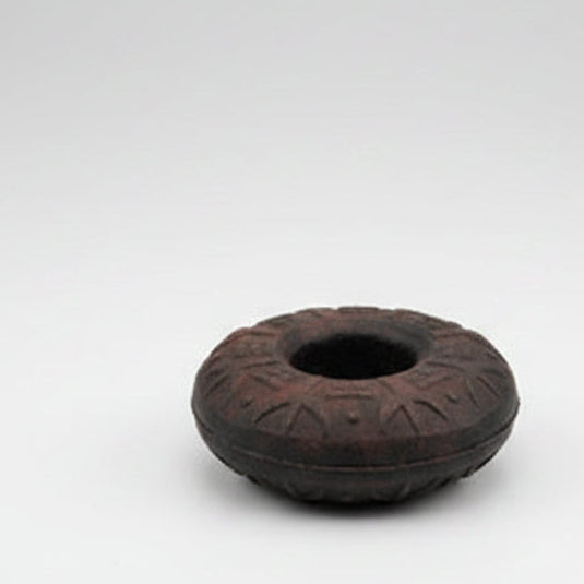 A dark-colored metal finger bell with embossed patterns and a central hole for wearing on a finger.