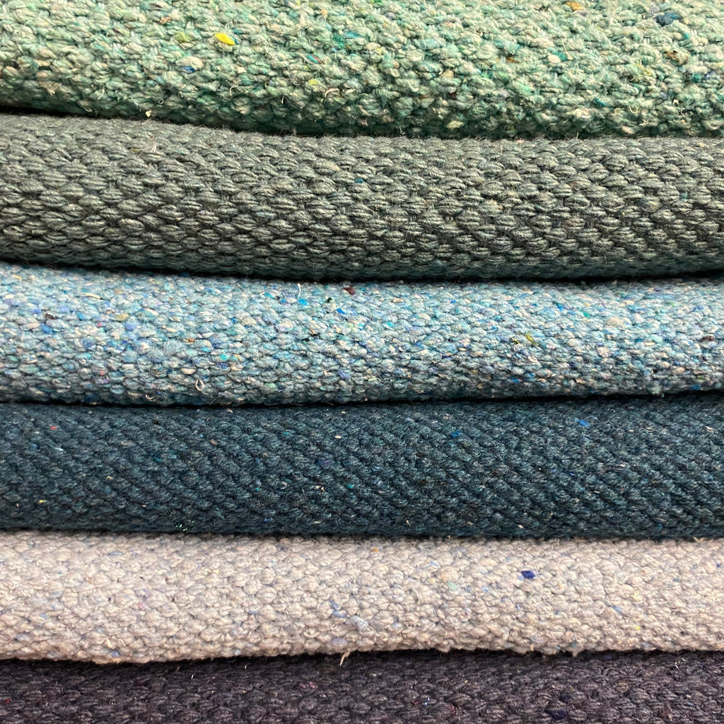 A stack of various colored rectangular rugs, with a focus on a green rug at the top.