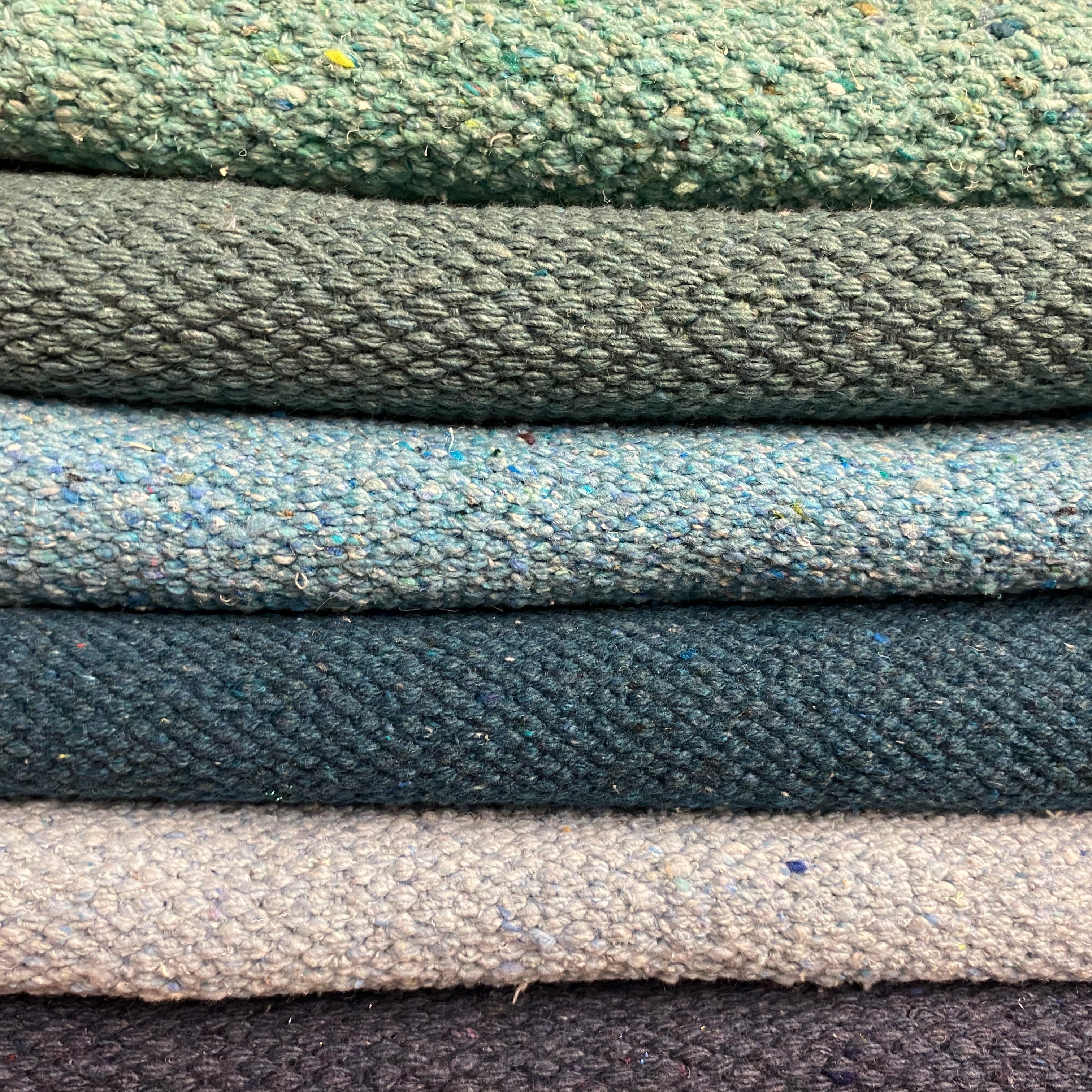 A stack of various colored rectangular rugs, with a focus on a green rug at the top.