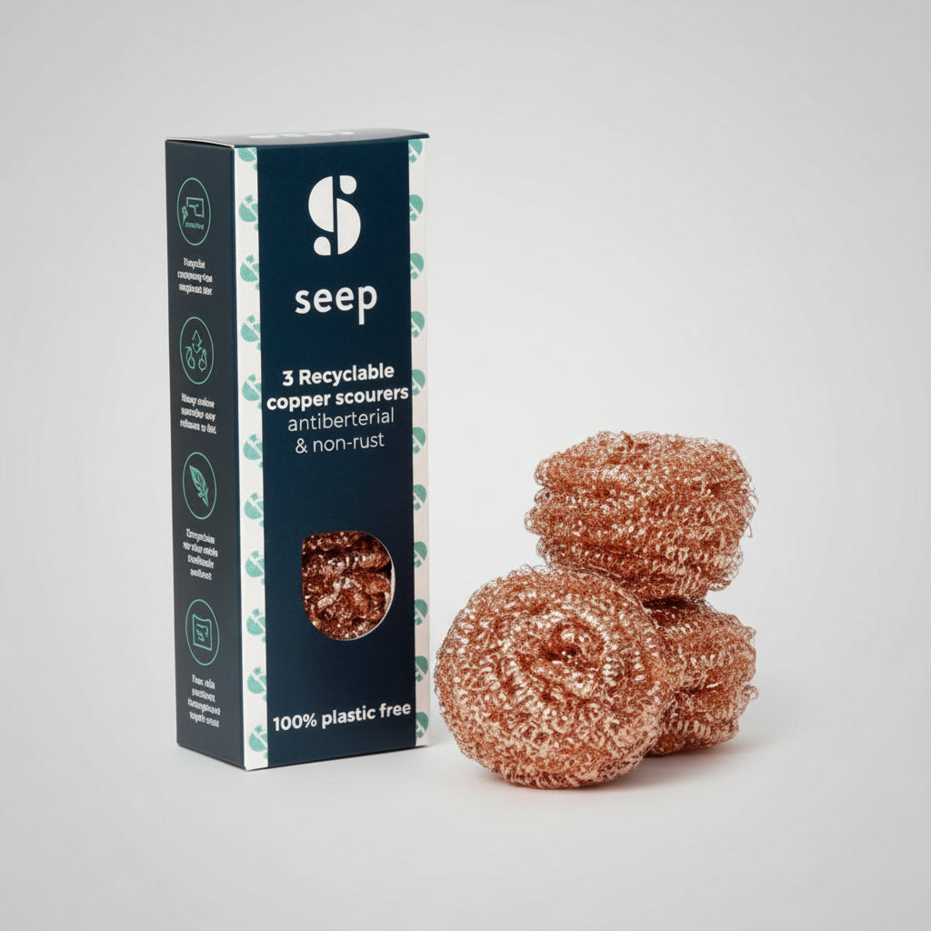 A pack of three recyclable copper scourers next to their packaging, which is labeled as 100% plastic-free.
