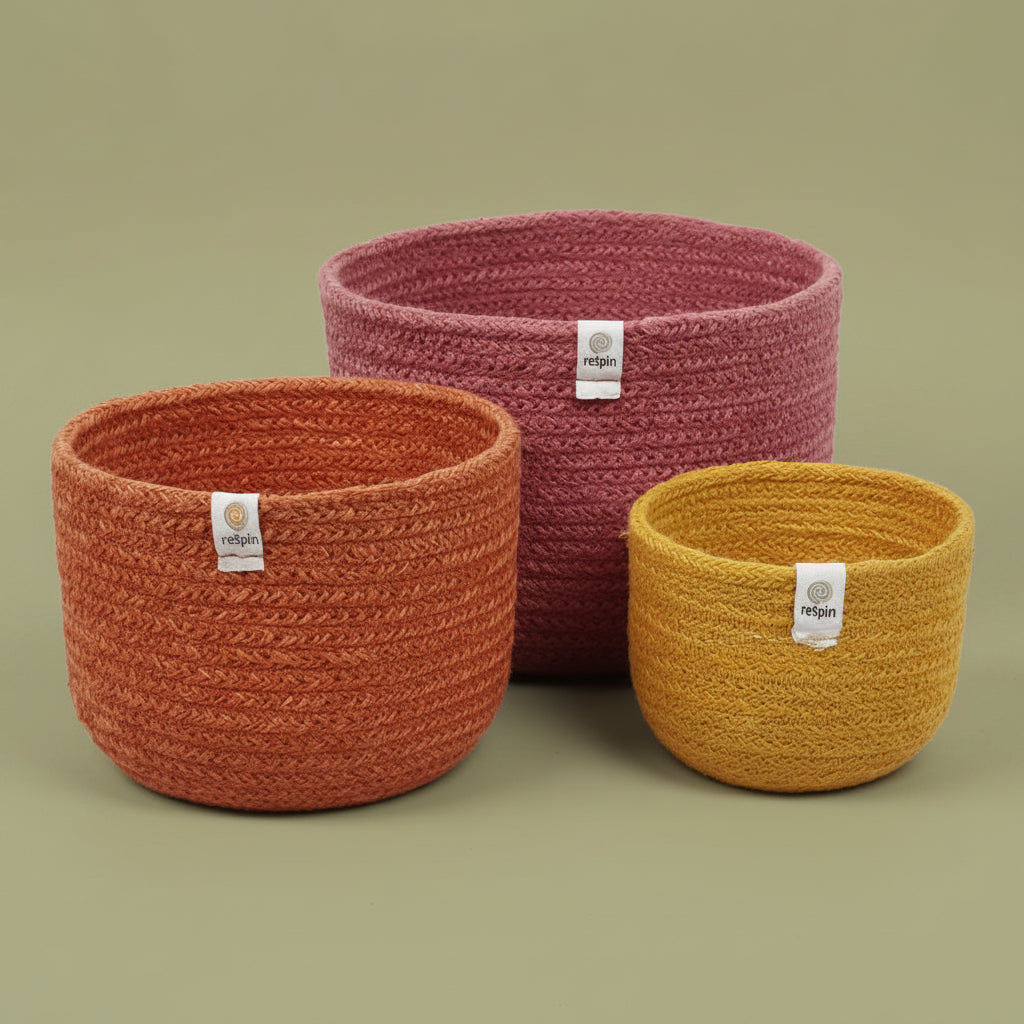 A set of three jute baskets in small, medium, and large sizes, in shades of brown and yellow, with a tag displaying 'Handmade in Bangladesh'.